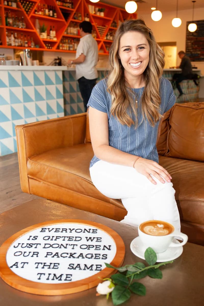 Molly seated behind a sign that reads Everyone is gifted, we just don't open our packages at the same time